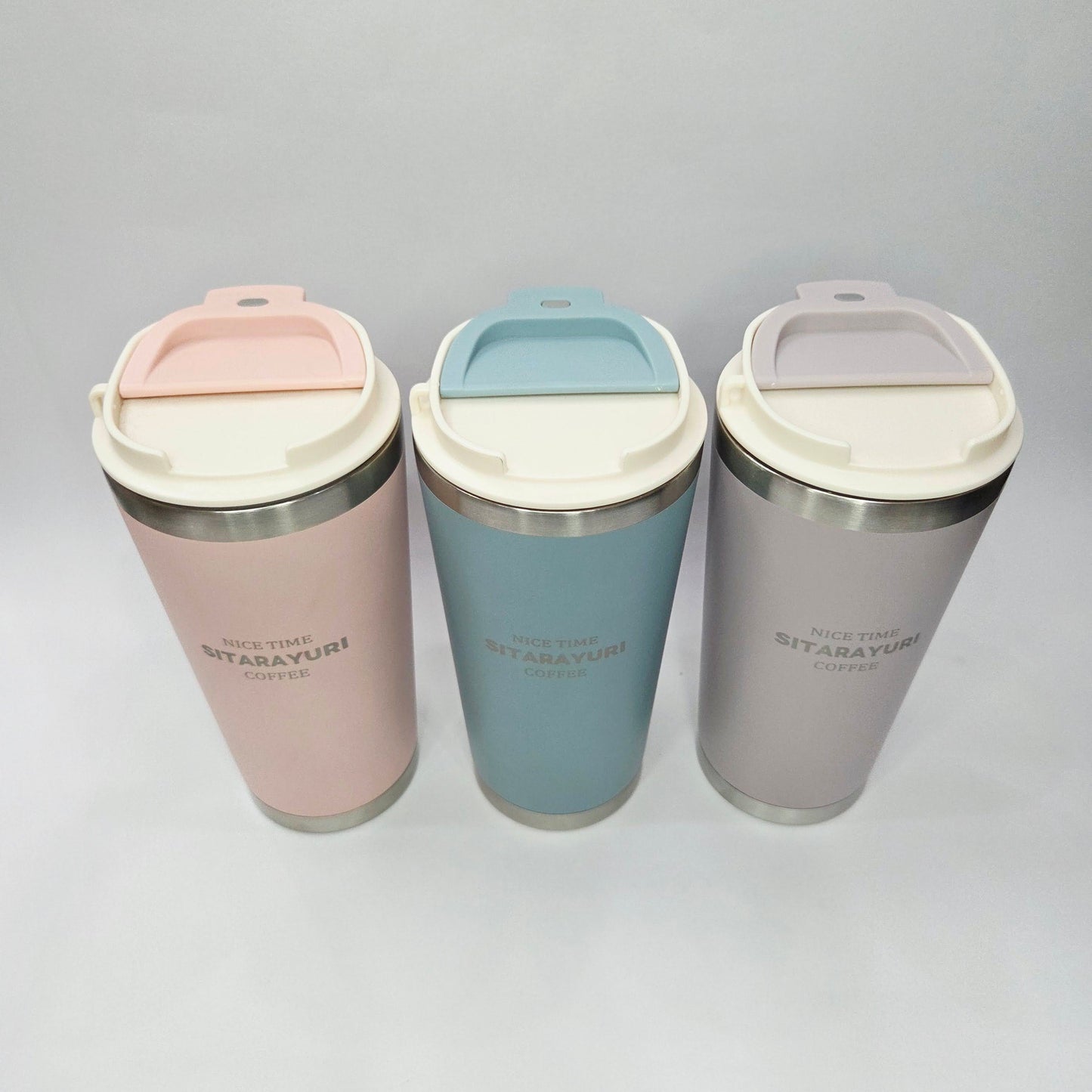 Three insulated travel mugs in gray, blue, and pink on a light gray background